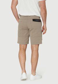 Pantalones cortos beige hechos de un tejido texturizado, con un parche negro en la cintura. El diseño incluye bolsillos laterales y un dobladillo de longitud moderada.