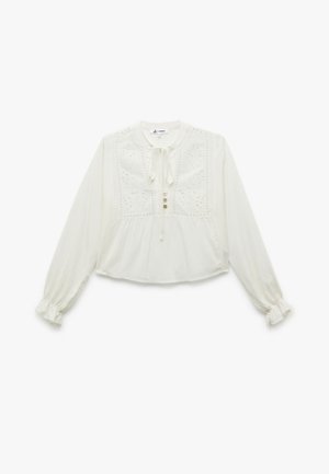 Blusa bianca a maniche lunghe con scollo rotondo, dettaglio a fiocco, ricamo floreale sulla parte anteriore e chiusura con bottoni. Tessuto morbido e strutturato.