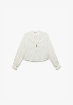 Blusa blanca de manga larga con escote redondo, detalle de lazo, bordado floral en el frente y cierre de botón. Tejido suave y texturizado.