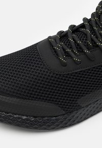 Černá sportovní bota s síťovaným svrškem a polstrovaným jazykem. Obsahuje reflexní žluté akcenty na tkaničkách. Texturovaná černá gumová podešev.