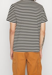 T-shirt rayé avec des bandes horizontales noires et crème, manches courtes et col rond, associé à un short cargo orange.