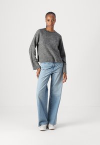 Pull en tricot gris à manches longues, coupe décontractée et fentes latérales ; associé à un jean large bleu clair et des baskets blanches.
