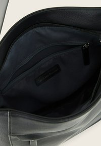 Interno di una borsa in pelle nera, con una texture liscia, due tasche con zip e un'etichetta con marchio. Foderata in tessuto scuro.