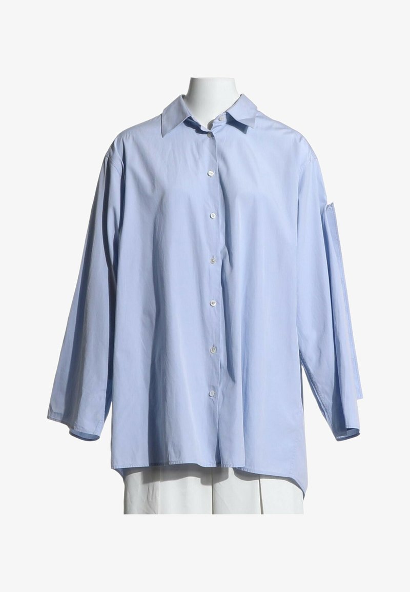 Chemise oversize bleu clair à boutons, manches longues et col standard, présentée sur un mannequin sans tête.