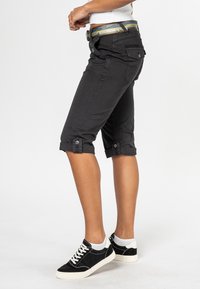 Zwarte capri-broeken met opgerolde manchetten, zijzakken en knoopdetails. Gecombineerd met zwarte sneakers met witte accenten.