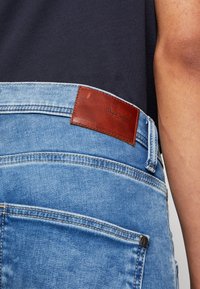 Ljusblå denimjeans med en brun läderetikett med präglad text vid midjan, synlig sömnad och en klassisk passform.