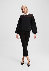Sweatshirt noir avec une partie supérieure transparente et un col blanc, associé à un pantalon noir court et des chaussures noires pointues.