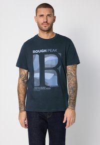 Marinblå bomulls-t-shirt med ett grafiskt tryck som visar "ROUGH PEAK" och abstrakta former. Korta ärmar och rund halsringning.