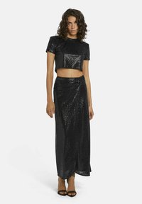 Zwart pailletten crop top en lange rok set, met een aansluitende silhouet en een gestructureerd oppervlak, gecombineerd met zwarte enkelband hakken.