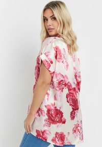 Silkesblus med stort rosa och rött blommönster på en ljus krämig bakgrund, korta uppvikta ärmar och en avslappnad passform.