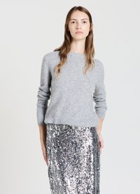 Grauer gestrickter Pullover aus weichem Material mit rundem Ausschnitt und langen Ärmeln, kombiniert mit einem silbernen Paillettenrock für einen strukturierten Look.