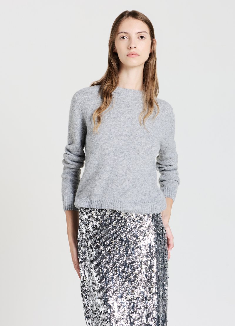 Grauer gestrickter Pullover aus weichem Material mit rundem Ausschnitt und langen Ärmeln, kombiniert mit einem silbernen Paillettenrock für einen strukturierten Look.