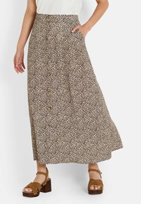 Falda midi de leopardo con un frente de botones, bolsillos y una silueta en A. La tela es ligera y de textura suave. Sandalias de plataforma marrones.