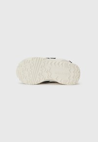 Semelle de sneaker en caoutchouc blanc avec un motif de semelle robuste et un logo en relief, avec un upper noir contrastant visible en haut.