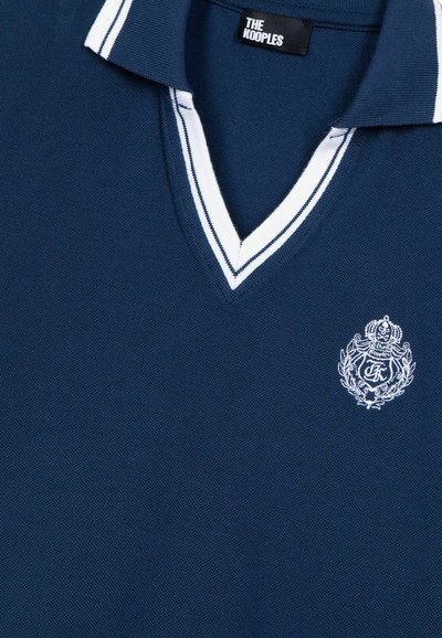 Marineblå polo-shirt med hvid V-hals og stribe. Har et broderet logo på brystet. Tekstureret stof med en klassisk pasform.