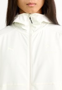 Chaqueta deportiva blanca con cuello alto, cierre de cremallera en el frente y logotipos: Puma y BMW Motorsport. Textura suave y material ligero.