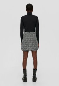 Svart polotröja och texturerade grå vävda shorts med hög midja och veck. Svarta grova ankelstövlar fulländar outfiten.