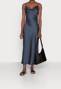 Robe en satin navy à pois blancs, avec un corsage ajusté et des bretelles spaghetti ; assortie à un sac à main noir texturé et des sandales noires à glisser.