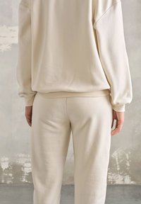 Beżowe dresy i dopasowana, oversize'owa bluza z miękkiego materiału, z prążkowanymi mankietami i pasem. Minimalistyczny design bez wzorów.