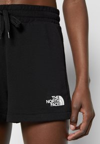 Gros plan d'une personne portant un short noir à taille élastique avec un cordon et le logo The North Face sur la jambe gauche.