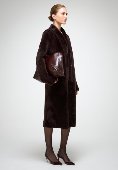 Garš tumši brūns mākslīgās kažokādas mētelis ar šalli apkakli, kombinēts ar tumši sarkanas ādas somiņu un melnas caurspīdīgas zeķubikses. Norādīta purngalu papēži.