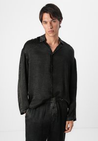 Chemise noire à boutons avec un tissu texturé et froissé, à manches longues et col, assortie à un pantalon décontracté à coupe ample.
