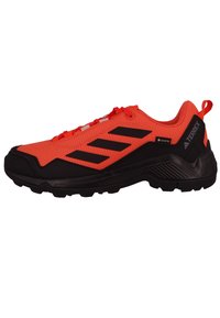 Pomarańczowe buty sportowe z czarnymi akcentami, z fakturowaną cholewką, wzmocnionym czubkiem i przyczepną podeszwą. Posiadają sznurowane zapięcie oraz wyściełany kołnierz.