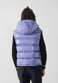 Pufferbodywarmer van glanzend lavendel materiaal met een capuchon, voorzien van doorgestikte secties en een getailleerd ontwerp. Zwart topje met lange mouwen eronder.