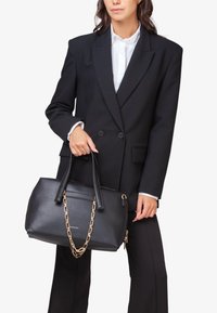 Zwarte leren handtas met dubbele handvatten en een gouden kettingaccent. Het heeft een gestructureerd oppervlak, een ritssluiting en een slanke silhouet.