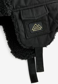 Gilet nero trapuntato con un interno morbido e testurizzato. Include una tasca frontale con un logo geometrico dorato e cinghie regolabili.