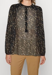 Černá průhledná blůza s béžovým skvrnitým vzorem, s límečkem a knoflíkovou légou. Dlouhé nařasené rukávy.