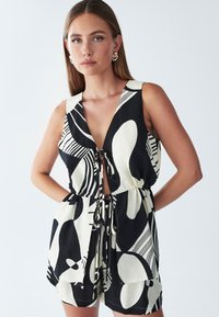 Czarnobiały kombinezon w wzory z głębokim dekoltem w serek i wiązaniem w talii. Posiada abstrakcyjne kształty i paski, wykonany z lekkiego materiału.