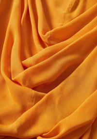 Tissu orange doux avec de légers plis et une couture visible, créant une texture lisse et fluide ainsi qu'une certaine dimension.