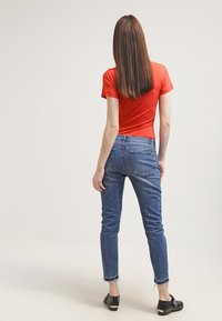 T-shirt rossa, design aderente, abbinata a jeans skinny blu con orlo sfrangiato. Scarpe nere completano l'outfit.