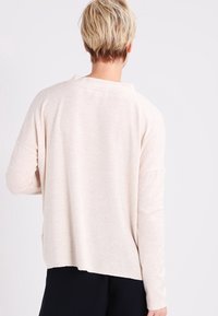 Ljusbeige oversized tröja i mjukt stickat material. Har långa ärmar, rundad nederkant och detalj vid bakhalsen.