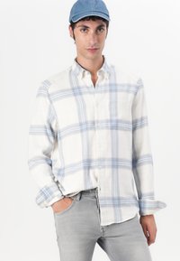 Kortermet, lett, hvit skjorte med blå rutemønster, knappeåpning, krage og frontlomme, kombinert med grå jeans.