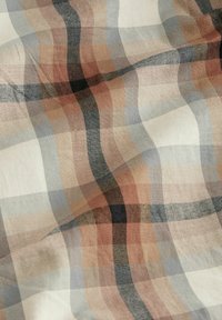 Tejido con un suave patrón de cuadros en tonos beige, marrón, negro y gris, que muestra una textura de tejido visible y suaves pliegues.