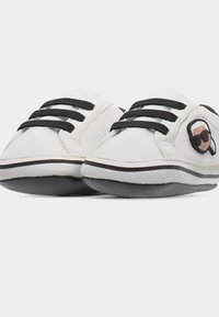 Λευκά παιδικά παπούτσια με μαύρα κορδόνια και σόλες, με ένα μικρό καρικατούρα πρόσωπο με γυαλιά ηλίου στο πλάι.