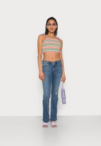 Top cropped de malha multicolorido com alças roxas, jeans de denim azul, mala lavanda e sandálias lilás claras. Textura suave e design ajustado.