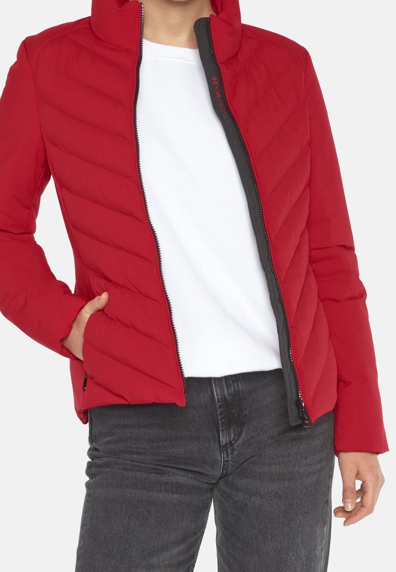 Chaqueta acolchada roja con cuello alto, cierre de cremallera y detalles en gris. Cuenta con un bolsillo lateral y textura suave. Se lleva sobre una camisa blanca.