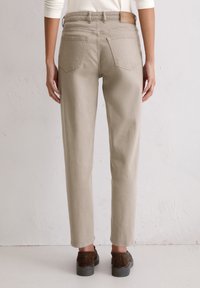 Light beige trousers with a straight-leg design, two back pockets, and a subtle textured finish. Accented with a brown leather waistband.