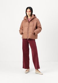 Brun puffjakke med hette, med glidelås foran og firkantet quiltet mønster. Kombinert med burgunder vide cordbuksene og beige leiligheter.