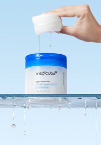 Medicube Zero Pore Pad-behållare med blått lock, genomskinlig kropp och flytande pads. Droppande fukt; märkt ingredienslista synlig på framsidan.