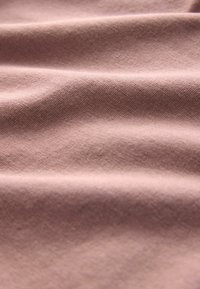 Textilstoff mit einer glatten Textur in einem sanften Mauve-Ton, der subtile diagonale Webmuster und sanfte Drapierungseffekte zeigt.