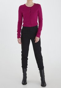 Różowy sweter na guziki z długimi rękawami, zestawiony z czarnymi spodniami z wysokim stanem i czarnymi kozakami za kolano. Gładka faktura materiału.