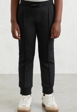 Mustat verkkarit, joissa on sivusaumat, joustava vyötärö ja nilkkasaumat, yhdistettyinä valkoisiin tennareihin. Sileä pinta, muotoiltu malli.