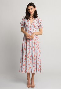 Kwiatowa sukienka midi w jasnoniebieskim materiale z różowymi i zielonymi wzorami kwiatowymi. Posiada bufiaste rękawy i głęboki dekolt w kształcie litery V. Noszona z sandałami na obcasie.