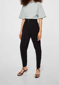 Blusa azzurro chiaro a maniche corte con scollatura decorativa, abbinata a pantaloni neri a vita alta e sandali neri con cinturini.