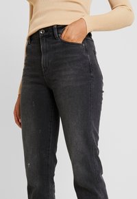Jeans de denim negro con un corte ajustado, que presentan un diseño clásico de cinco bolsillos, un ligero desvanecimiento y detalles desgastados en la parte frontal.