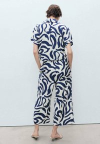 Košile s krátkým rukávem a široké kalhoty v krémové barvě s námořnickým vlnitým vzorem. Materiál vypadá lehký, má volný střih a elastický pas.